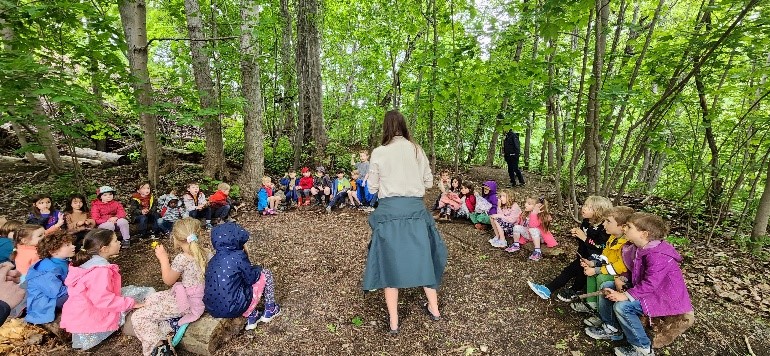 A group of children sitting in a forest
Description automatically generated