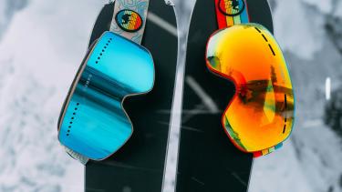 Two skis stuck into the snow with goggles hanging from the tips.