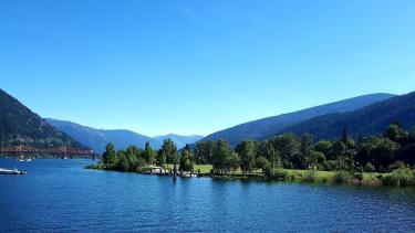 A blue lake with a treed park and mountains in the distance on a brilliant, blue-sky sunny day